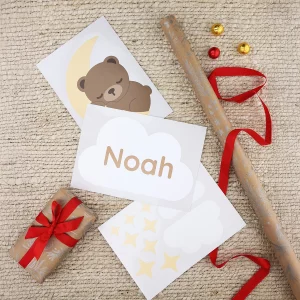Oviin tarkoitettuja tarroja arkilla, jossa on karhu, joka nukkuu kuun päällä, sekä pilvi, jossa lukee "Noah", joulupaperin ympäröimänä.