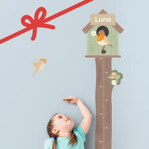 Lapsi mittaamassa pituuttaan puun muotoisesta kasvumittarista, jossa on linnunpönttö ja nimi ”Luna”.