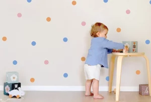Taapero leikkii värikkäästi koristellussa lastenhuoneessa, jossa on hauska pilkullinen seinätarra.