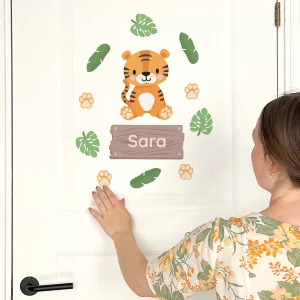 Suloinen tiikeriaiheinen lastenhuoneen ovitarra, jonka ympärillä on vihreitä lehtiä ja tassunjälkiä. Tekstinä Sara. Täydellinen henkilökohtainen sisustusratkaisu lapsille.