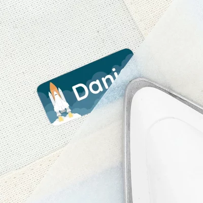 Personoitu silitettävä nimilappu raketin kuvalla tekstiilille kiinnitettynä.