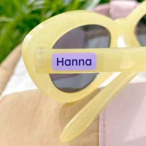 Keltainen aurinkolasit, joissa on violetti minitarra tekstillä Hanna. Täydellinen tuote pinempiin esineisiin, helppo kiinnittää ja tyylikäs ulkonäkö.