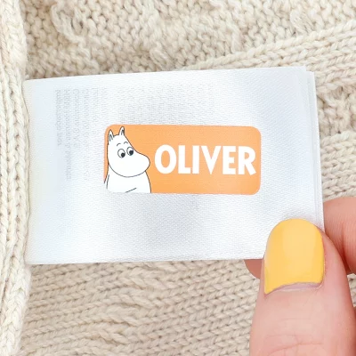 Vaatteen pesumerkintälappuun kiinnitetty Muumi-nimitarra, jossa tekstinä "Oliver". Täydelliset lastenvaatteisiin.