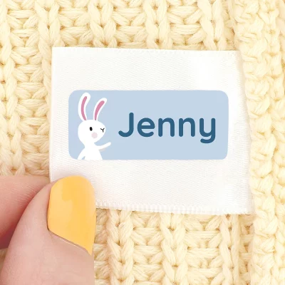 Vaatteen pesumerkintälappuun kiinnitetty sininen nimitarra, jossa pupun kuva ja teksti "Jenny".
