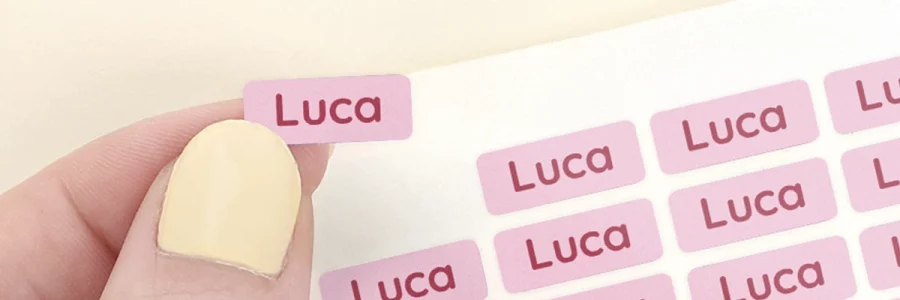 Arkillinen vaaleanpunaisia minitarroja tekstillä "Luca". Minitarrat kiinnitettyinä lyijykyniin.