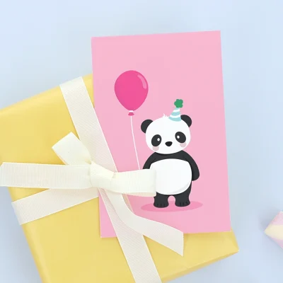 Syntymäpäiväkortti, jossa on suloinen panda, joka pitää vaaleanpunaista ilmapalloa. Kortti on asetettu keltaisen lahjapaketin päälle, joka on koristeltu valkoisella nauhalla. Tämä kortti on täydellinen lisä syntymäpäivälahjoihin lapsille.