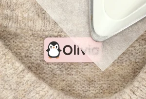 Nimiä etiketti, jossa on pingviini-kuvio ja nimi Olivia, asetettuna pehmeän taustatekstiilin päälle. Täydellinen valinta lasten vaatteiden ja tavaroiden merkitsemiseen.