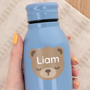Personoitu sininen juomapullo, jossa on söpö karhun kuva ja nimi Liam. Pullo on käsissä ja taustalla näkyy vaaleaa kangasta, mikä giruuttaa esille lasten tuotteiden ystävällisen ja leikkisän tunnelman. Tämä tuote on täydellinen lahjaidea lapsille ja sopii erinomaisesti myös koulun käyttöön.